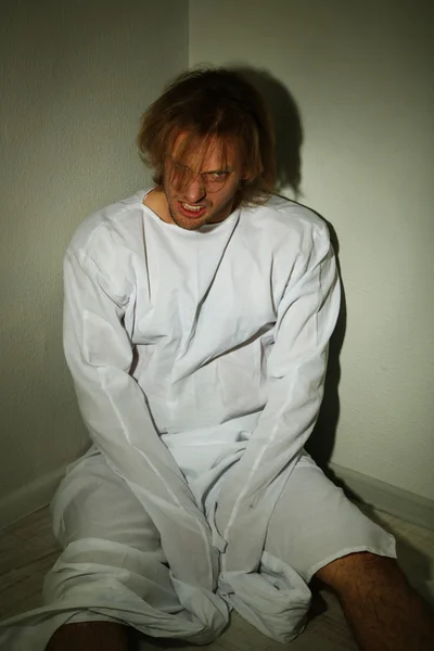 Психически больной человек в смирительной рубашке в углу комнаты — стоковое фото