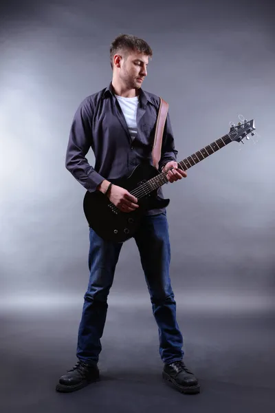 Joven músico tocando la guitarra sobre fondo gris — Foto de Stock