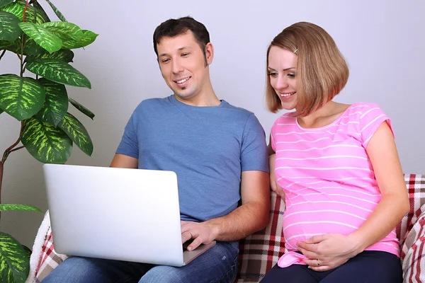 年轻孕妇和她的丈夫抱着笔记本电脑在家里的沙发上 — 图库照片