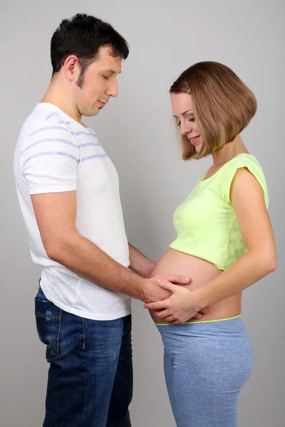 Jeune femme enceinte avec son mari sur fond gris彼女の夫と灰色の背景で若い妊娠中の女性 — ストック写真