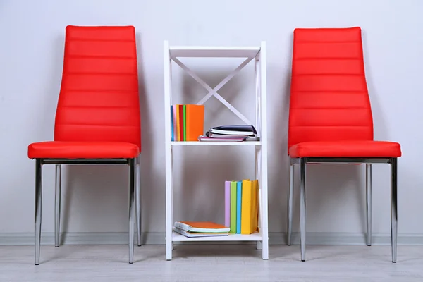 Beautiful interior with modern color chairs, books on wooden stand, on wall background — Stock Photo, Image