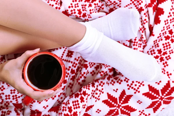 Kompozycja z ciepły pled, filiżanka gorący napój i kobiece nogi, na tle dywan kolor — Zdjęcie stockowe