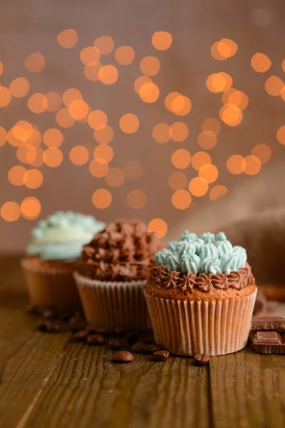 Cupcakes saborosos com creme de manteiga, na mesa de madeira, no fundo luzes — Fotografia de Stock