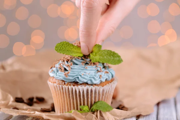 Female hand decorating tasty cupcake with butter cream, on color wooden table, on lights background — Stock Photo, Image