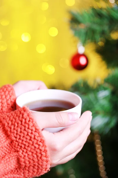 Mãos segurando caneca de bebida quente, close-up, no fundo da árvore de Natal — Fotografia de Stock
