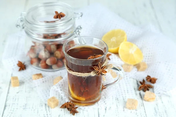 Hot beverage in glass cup with fruits and spices, on wooden background — Stock Photo, Image