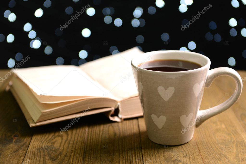 Composition of book with cup of coffee on table on dark background