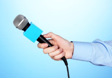 Erkek el ile mavi arka plan üzerinde mikrofon
