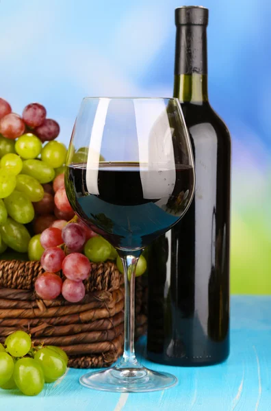 Ripe green and purple grapes in basket with wine on wooden table on natural background — Stock Photo, Image