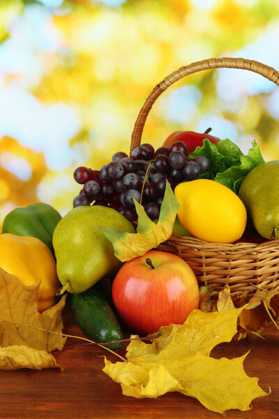 Different fruits and vegetables with yellow leaves in basket on table on bright background