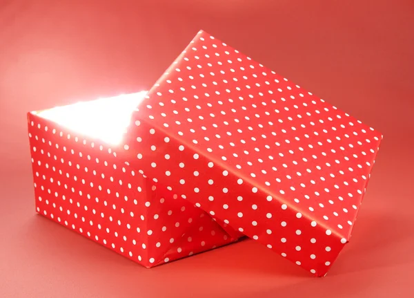 Caja de regalo con luz brillante sobre fondo rojo — Foto de Stock