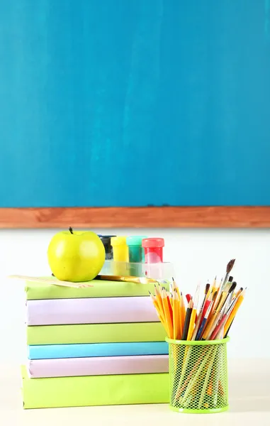 School supplies on table on blackboard background — Stock Photo, Image