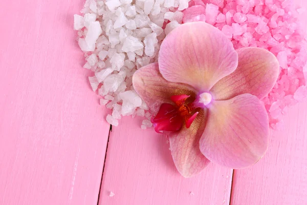 Beautiful blooming orchid flower and heap of sea salt, on color wooden background — Stock Photo, Image