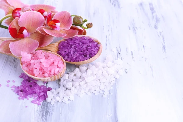 Bodegón con hermosa flor de orquídea y cucharas de madera con sal marina, sobre fondo de madera de color —  Fotos de Stock