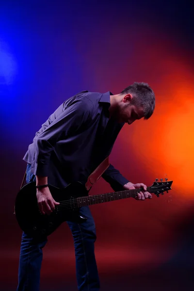 Joven músico tocando la guitarra sobre fondo de color oscuro — Foto de Stock