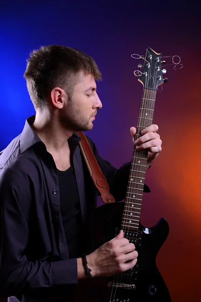 Joven músico tocando la guitarra sobre fondo de color oscuro —  Fotos de Stock