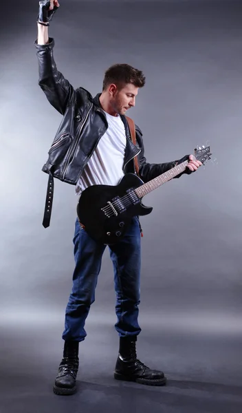 Joven músico tocando la guitarra sobre fondo gris — Foto de Stock