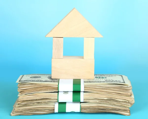 Wooden house on packs of dollars on blue background — Stock Photo, Image