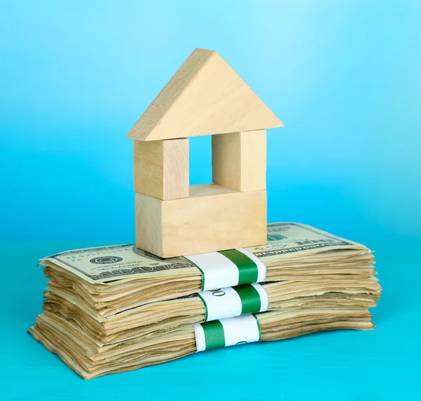 Wooden house on packs of dollars on blue background — Stock Photo, Image