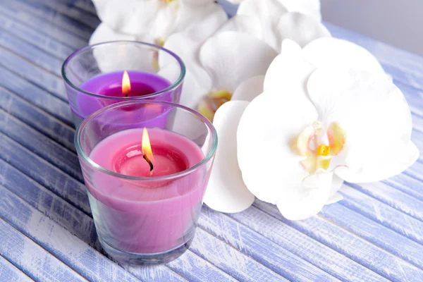 Schöne bunte Kerzen und Orchideenblumen, auf farbigem Holztisch, auf hellem Hintergrund — Stockfoto
