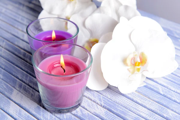 Hermosas velas de colores y flores de orquídea, sobre mesa de madera de color, sobre fondo claro —  Fotos de Stock