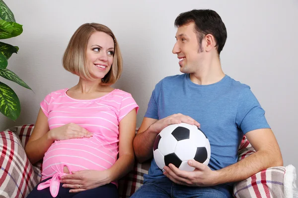 Young pregnant woman and her husband holding ball on sofa at home — Stock Photo, Image