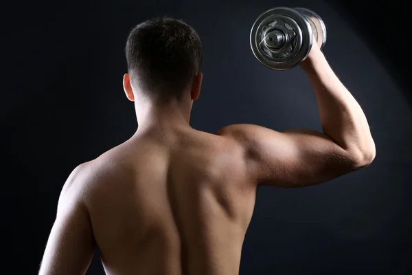 Красивый молодой мускулистый спортсмен выполняет упражнения с гантелями на темном фоне — стоковое фото