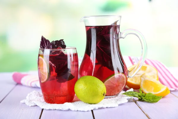 Limonata di basilico rosso in brocca e vetro, su tavolo di legno, su sfondo brillante — Foto Stock