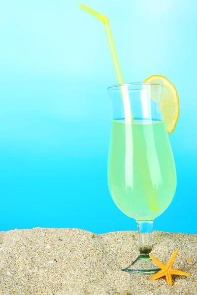 Beach cocktail in sand on blue background — Stock Photo, Image