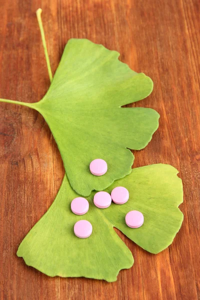 Ginkgo biloba leaves and pills on wooden background — Stock Photo, Image