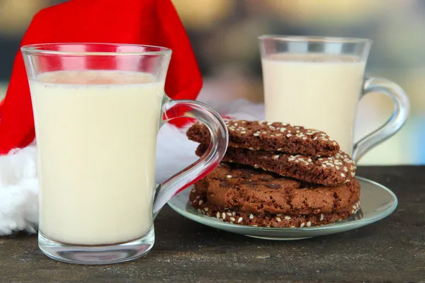 Copas de ponche de huevo con galletas y sombrero de Santa en la mesa sobre fondo brillante — Foto de Stock