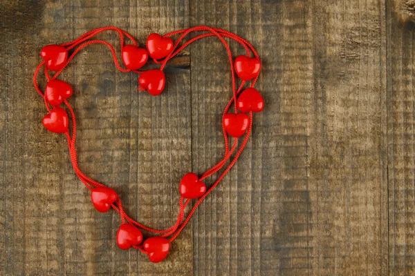 Heart-shaped beads on string on wooden background — Stock Photo, Image
