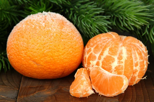Ripe frosted tangerines with fir branch on wooden background — Stock Photo, Image