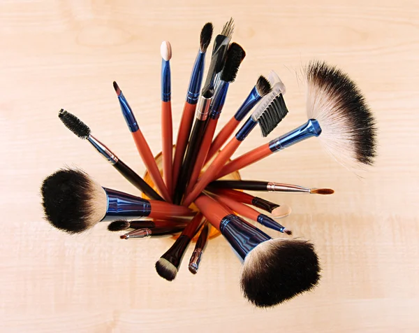 Makeup brushes in glass on wooden background — Stock Photo, Image