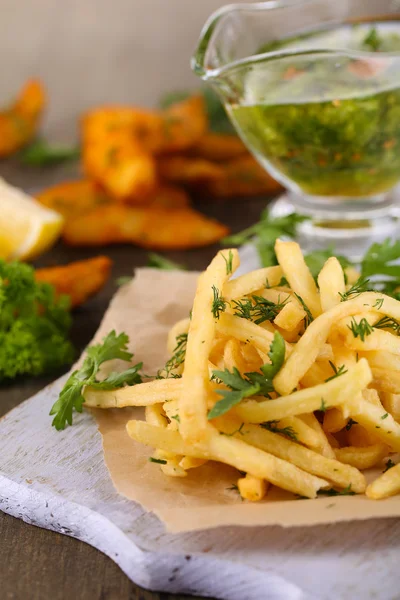 French fries on tracing paper on board on wooden table — Stock Photo, Image