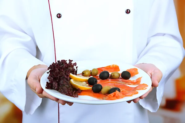 Fish on plate in cook hands on bright background — Stock Photo, Image