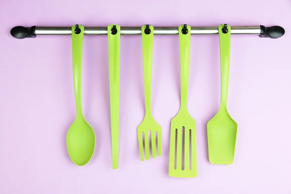 Plastic kitchen utensils on silver hooks on lilac background — Stock Photo, Image