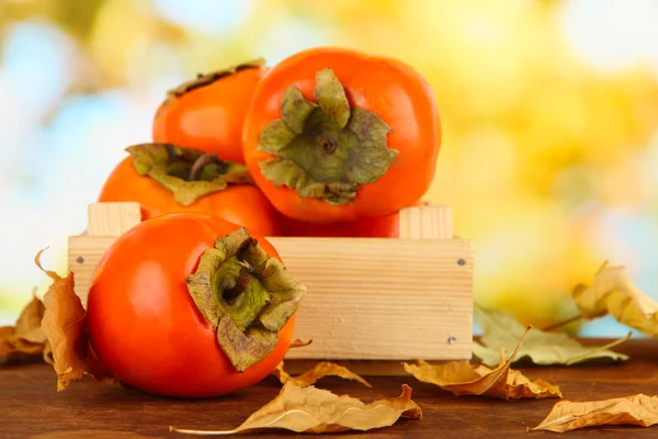 Ripe persimmons in crate on table on bright background — Stock Photo, Image