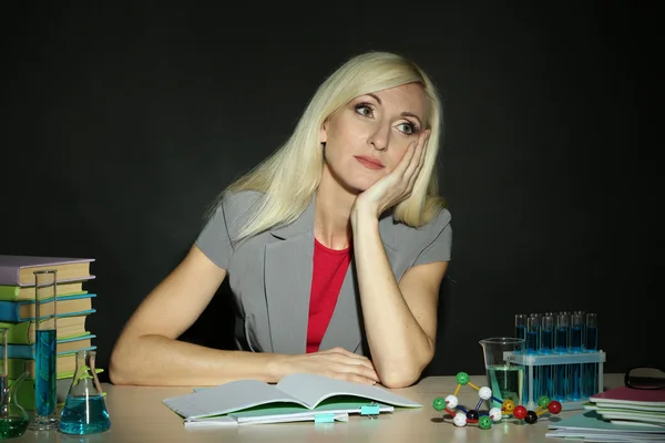 累了的化学老师坐在桌旁，在黑暗的彩色背景 — 图库照片