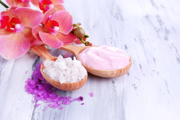 Bodegón con hermosa flor de orquídea y cucharas de madera con sal marina, sobre fondo de madera de color —  Fotos de Stock