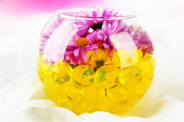 Hermosas flores en jarrón con hidrogel en la mesa sobre fondo brillante —  Fotos de Stock