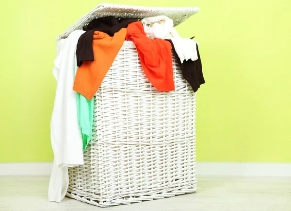 Full laundry basket on wooden floor on green wall background — Stock Photo, Image