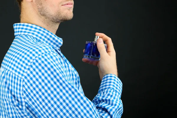 Bonito jovem usando perfume no fundo preto — Fotografia de Stock