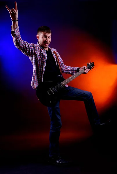 Joven músico tocando la guitarra sobre fondo de color oscuro — Foto de Stock