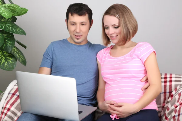 Young pregnant woman with her husband holding laptop on sofa at home — Stock Photo, Image