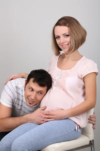 Young pregnant woman with her husband listening belly on gray background — Stock Photo, Image