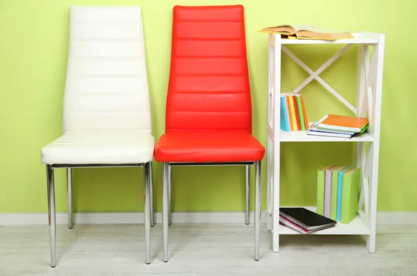 Bellissimo interno con sedie a colori moderne, libri su supporto in legno, su sfondo a parete — Foto Stock