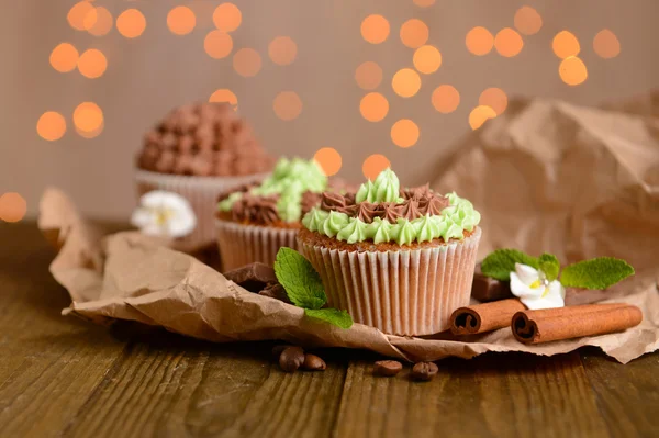 Ízletes cupcakes vaj tejszín, fából készült asztal, fények háttér — Stock Fotó