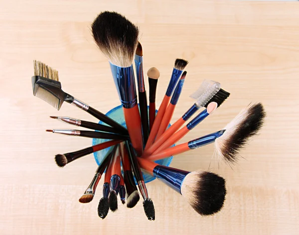Makeup brushes in glass on wooden background — Stock Photo, Image