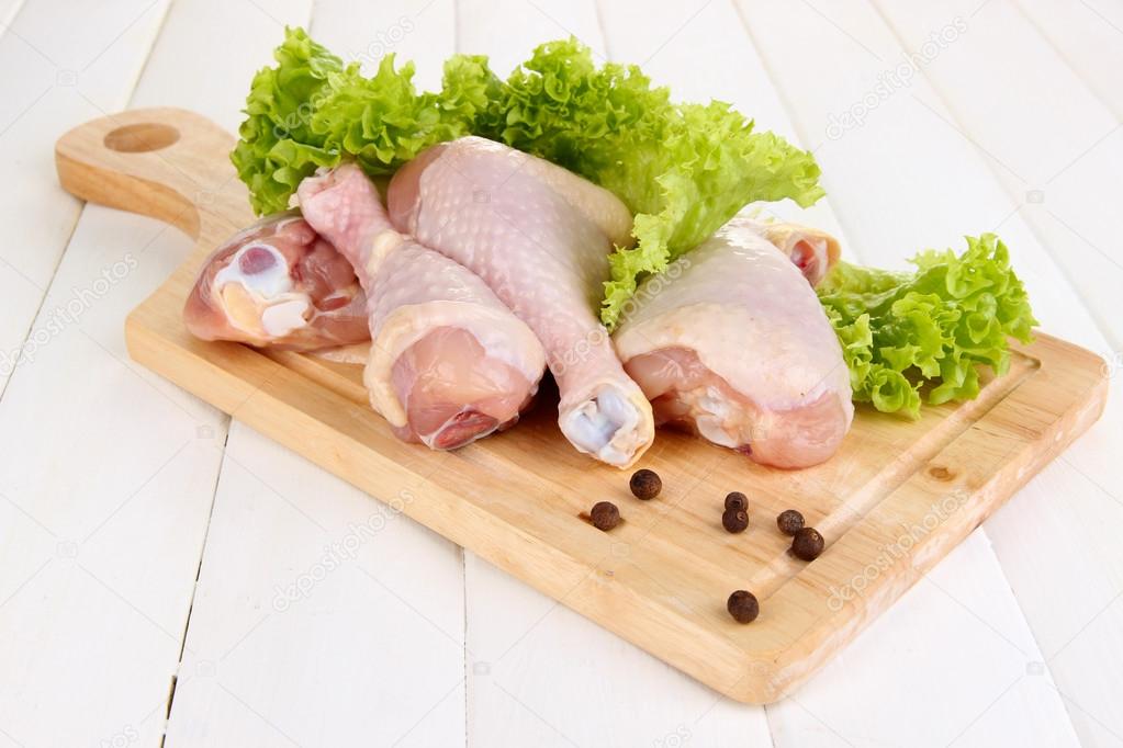 Raw chicken legs on wooden board on wooden table
